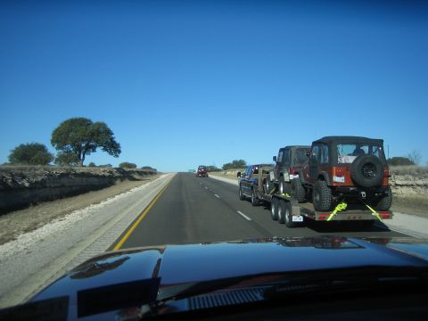 1996 Ford Bronco - Pickup truck towing a trailer with two Jeeps on a sunny day on the highway.