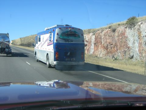 1996 Ford Bronco - A blue and white bus is seen from behind on a highway, emitting smoke, with a mural on its rear.