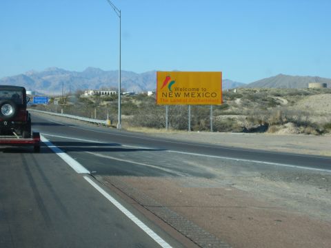 1996 Ford Bronco - A vehicle tows a trailer past the welcome sign for New Mexico, with mountains visible in the distance.