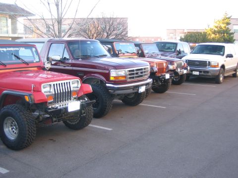 1996 Ford Bronco - A line of SUVs and trucks are parked in a lot, with a maroon Ford F-Series truck prominently featured in the foreground.