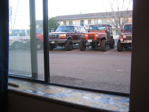 1996 Ford Bronco - Several off-road vehicles, including a 1996 Ford Bronco, are parked in a lot outside a building.
