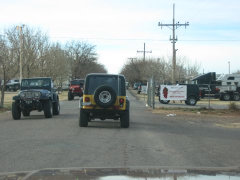 1996 Ford Bronco - Multiple Jeeps drive down a road towards a gate with a sign for a chili challenge.