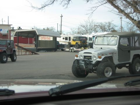 1996 Ford Bronco - Several off-road vehicles are parked in a lot, including a silver Toyota Land Cruiser and a maroon Jeep Wrangler.