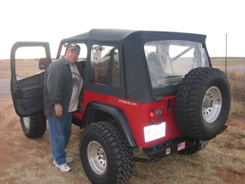 1996 Ford Bronco - A man stands next to a red Jeep Wrangler with its driver's door open and a spare tire mounted on the back.