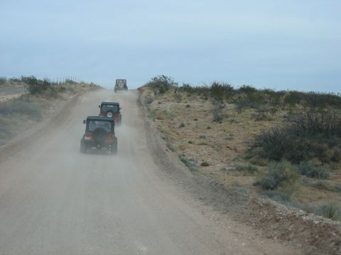 1996 Ford Bronco - Three Jeeps travel in single file on a dirt road, kicking up dust in a dry, arid environment.