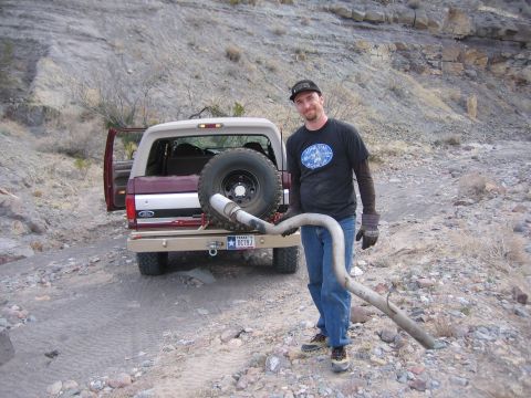 1996 Ford Bronco - A man stands with a removed exhaust pipe next to a Ford Bronco in a rocky, outdoor setting.