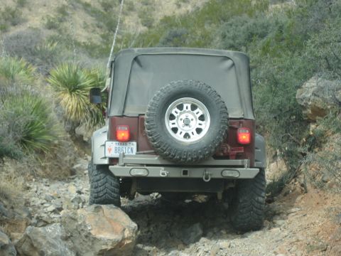1996 Ford Bronco - A maroon Jeep Wrangler navigates a rocky trail, its spare tire mounted on the back.