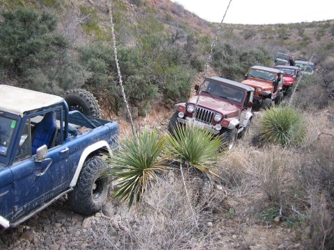 1996 Ford Bronco - A convoy of off-road vehicles navigates a , rocky trail through a dry, brushy landscape.