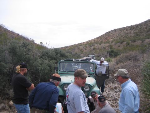 1996 Ford Bronco - A group of people inspect several vintage Jeeps on a rough, off-road trail in a desert landscape.
