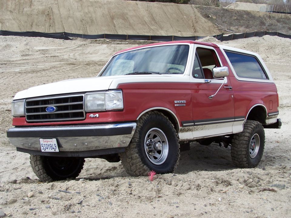 Red and white 1989 Ford Bronco 4x4 parked on sand
