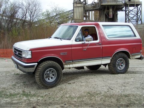1989 Ford Bronco - Red and white 1989 Ford Bronco with a driver visible through the window.