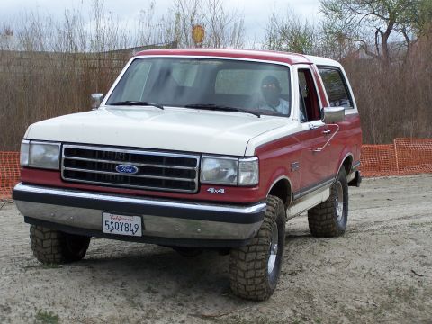 1989 Ford Bronco - This two-tone red and white Ford Bronco is equipped with off-road tires and appears to be in a dirt lot.