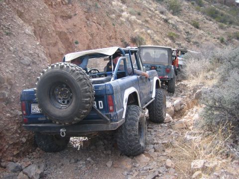 1996 Ford Bronco - A line of off-road vehicles, including a blue Ford Bronco, navigate a steep, rocky mountain path.