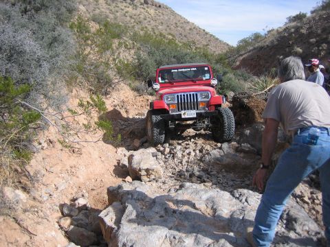 1996 Ford Bronco - A red Jeep navigates a rocky off-road trail with a person observing nearby.
