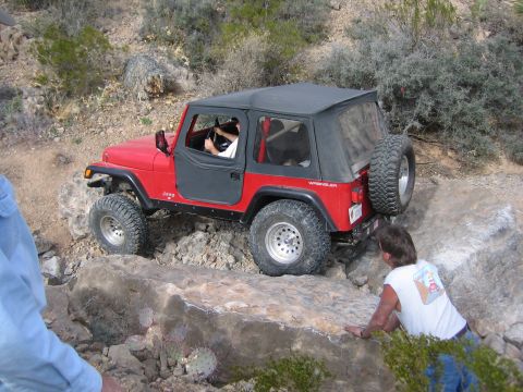 1996 Ford Bronco - Red Jeep Wrangler tackling a challenging off-road course with rocky obstacles.