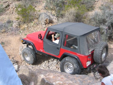 1996 Ford Bronco - A red Jeep Wrangler navigates a rocky off-road trail with a driver at the wheel.