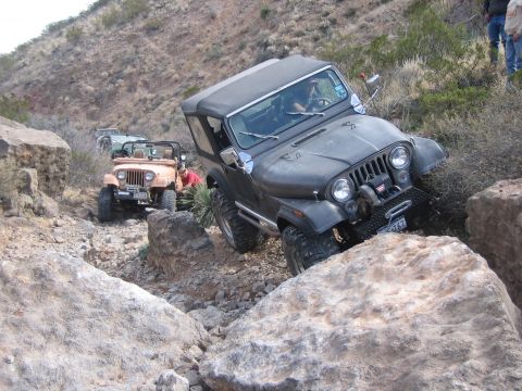 1996 Ford Bronco - Two Jeeps, a dark gray CJ-7 and a tan CJ-5, tackle a challenging rocky trail.