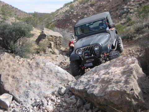 1996 Ford Bronco - A Jeep Wrangler TJ is shown off-roading on a rocky, desert-like terrain.