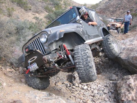 1996 Ford Bronco - A driver navigates a rocky off-road trail in a modified Jeep CJ-7, with another vehicle and onlookers nearby.