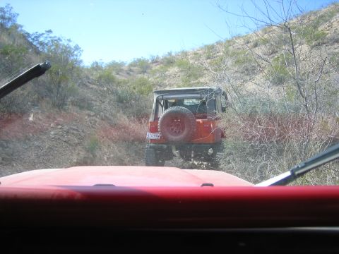 1996 Ford Bronco - Two off-road vehicles navigate a dusty trail through a barren, arid landscape under a clear blue sky.