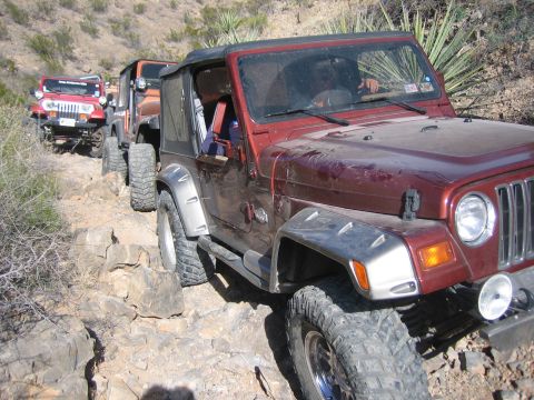 1996 Ford Bronco - Several Jeep Wranglers navigate a rocky trail in a desert landscape.