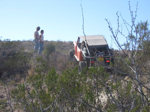 1996 Ford Bronco - An orange off-road buggy navigates a steep, rocky terrain under a clear blue sky.