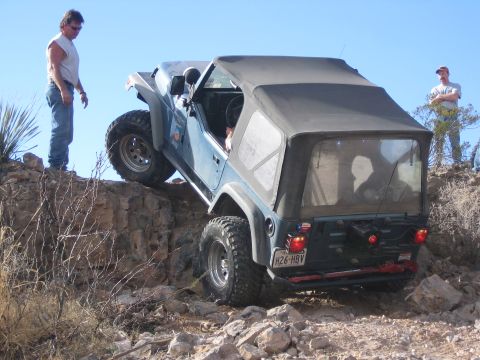 1996 Ford Bronco - Jeep Wrangler TJ navigating a steep, rocky incline with two people observing.