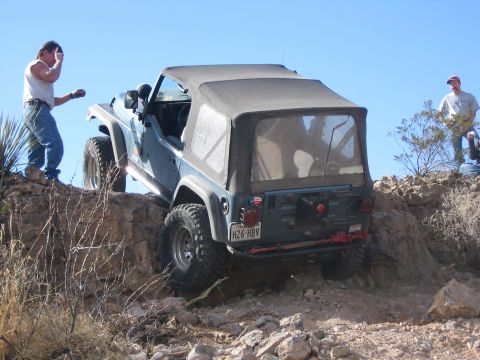 1996 Ford Bronco - A blue Jeep Wrangler navigates a steep, rocky incline under a clear blue sky.