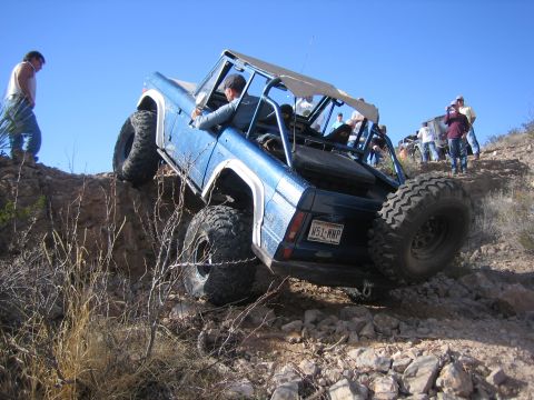 1996 Ford Bronco - A blue 1996 Ford Bronco navigates a steep, rocky trail with several spectators watching.