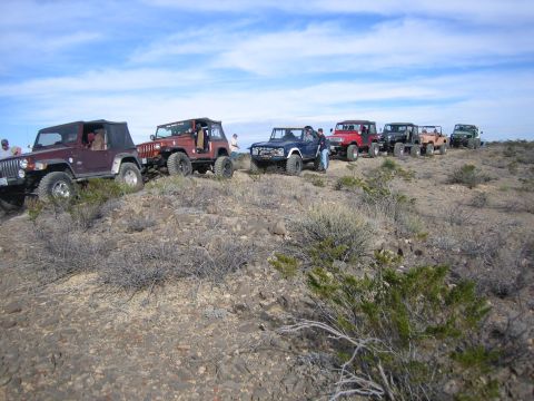 1996 Ford Bronco - A convoy of off-road vehicles is parked on a dusty, rocky terrain with sparse vegetation.