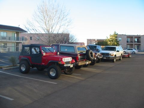 1996 Ford Bronco - Several vehicles are parked in a lot, including a red Jeep Wrangler and a white SUV with a trailer.