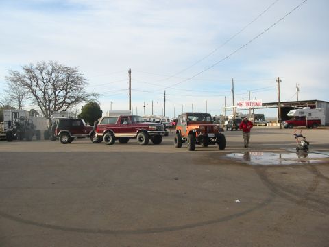 1996 Ford Bronco - Several off-road vehicles are parked in an outdoor lot under a cloudy sky.