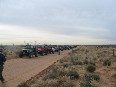 1996 Ford Bronco - A convoy of off-road vehicles travels down a dusty track in a dry, open landscape.
