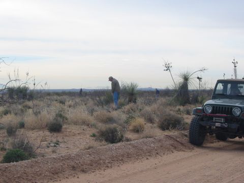 1996 Ford Bronco - Jeep Wrangler parked on a dirt road in a dry, desert landscape under a cloudy sky.