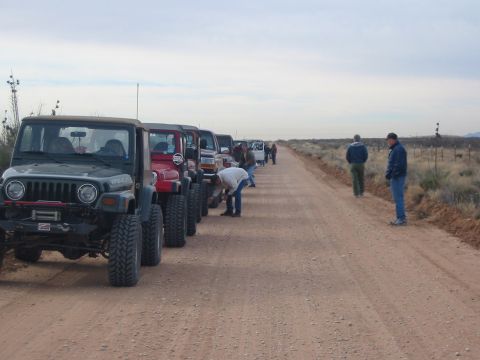 1996 Ford Bronco - A group of Jeeps are lined up on a dusty road, with several people gathered around them.