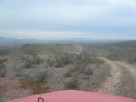 1996 Ford Bronco - Several SUVs traverse a dusty desert road, kicking up dust under a hazy sky with distant mountains.