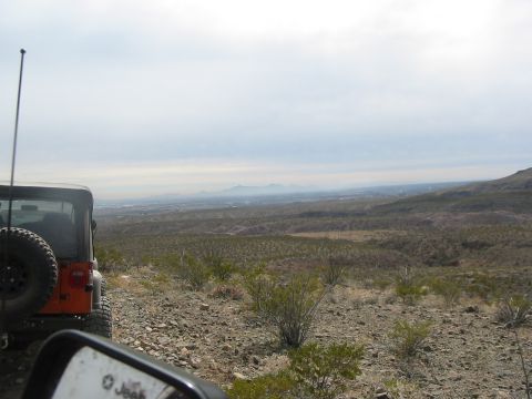 1996 Ford Bronco - An orange Jeep Wrangler is parked on a rocky hillside, its side mirror reflecting the Jeep logo, with a vast valley stretching out in the d…