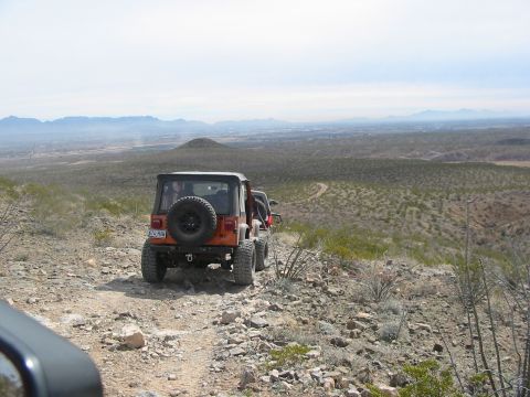1996 Ford Bronco - Two Jeeps navigate a rough desert trail with mountains in the distance.