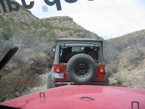 1996 Ford Bronco - Two Jeeps navigate a rocky trail through a desert canyon under a cloudy sky.