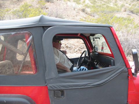 1996 Ford Bronco - A man drives a red Jeep Wrangler with a soft top through a dry, brushy landscape.