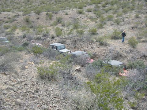 1996 Ford Bronco - Multiple off-road vehicles are parked in a line on a dry, rocky hillside. A person is walking in the background.