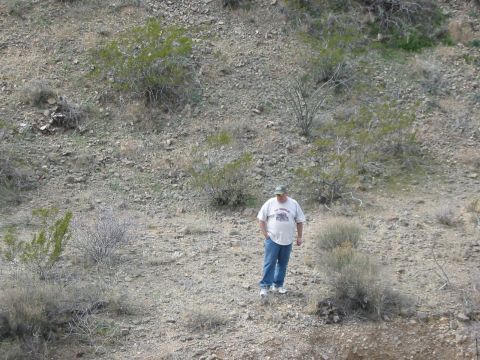 1996 Ford Bronco - A man stands in a desolate, rocky landscape dotted with dry brush and small green plants.