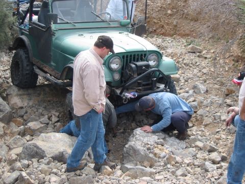 1996 Ford Bronco - A group of people inspect a green Jeep CJ-7 that is stuck on a rocky trail.