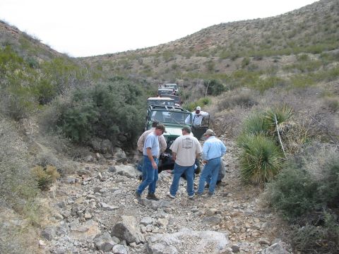 1996 Ford Bronco - A convoy of off-road vehicles makes its way through a challenging, rocky terrain, with several individuals observing the progress.