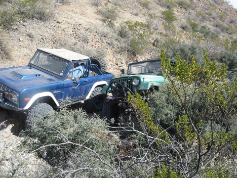 1996 Ford Bronco - Two off-road vehicles, a blue Ford Bronco and a green Jeep Wrangler, navigate a rocky trail.