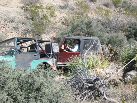 1996 Ford Bronco - Two off-road vehicles are seen traversing a , desert-like terrain with sparse vegetation.