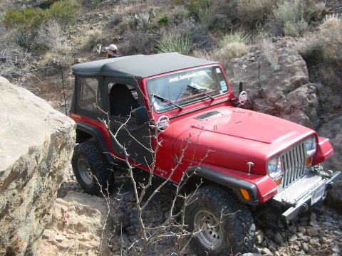 1996 Ford Bronco - A red Jeep Wrangler tackles a challenging off-road trail with rocky obstacles.