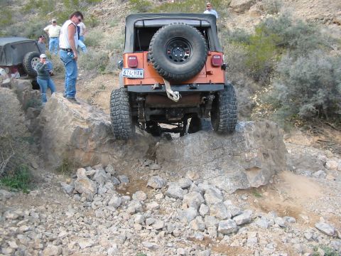 1996 Ford Bronco - An orange Jeep Wrangler navigates a rocky off-road trail with another vehicle visible in the background.