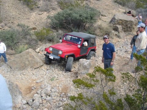 1996 Ford Bronco - A red Jeep Wrangler navigates a rocky off-road trail with several onlookers.
