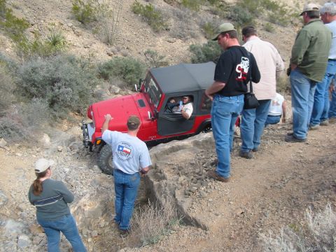 1996 Ford Bronco - A group of people observe a red Jeep Wrangler as it maneuvers through a challenging off-road path.